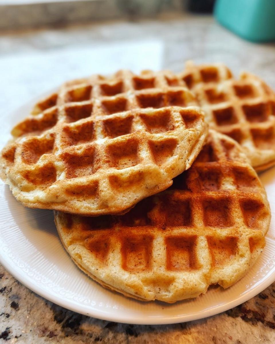 Close-up of three golden-brown homemade dog waffles stacked on a white plate, lightly dusted with cinnamon.
