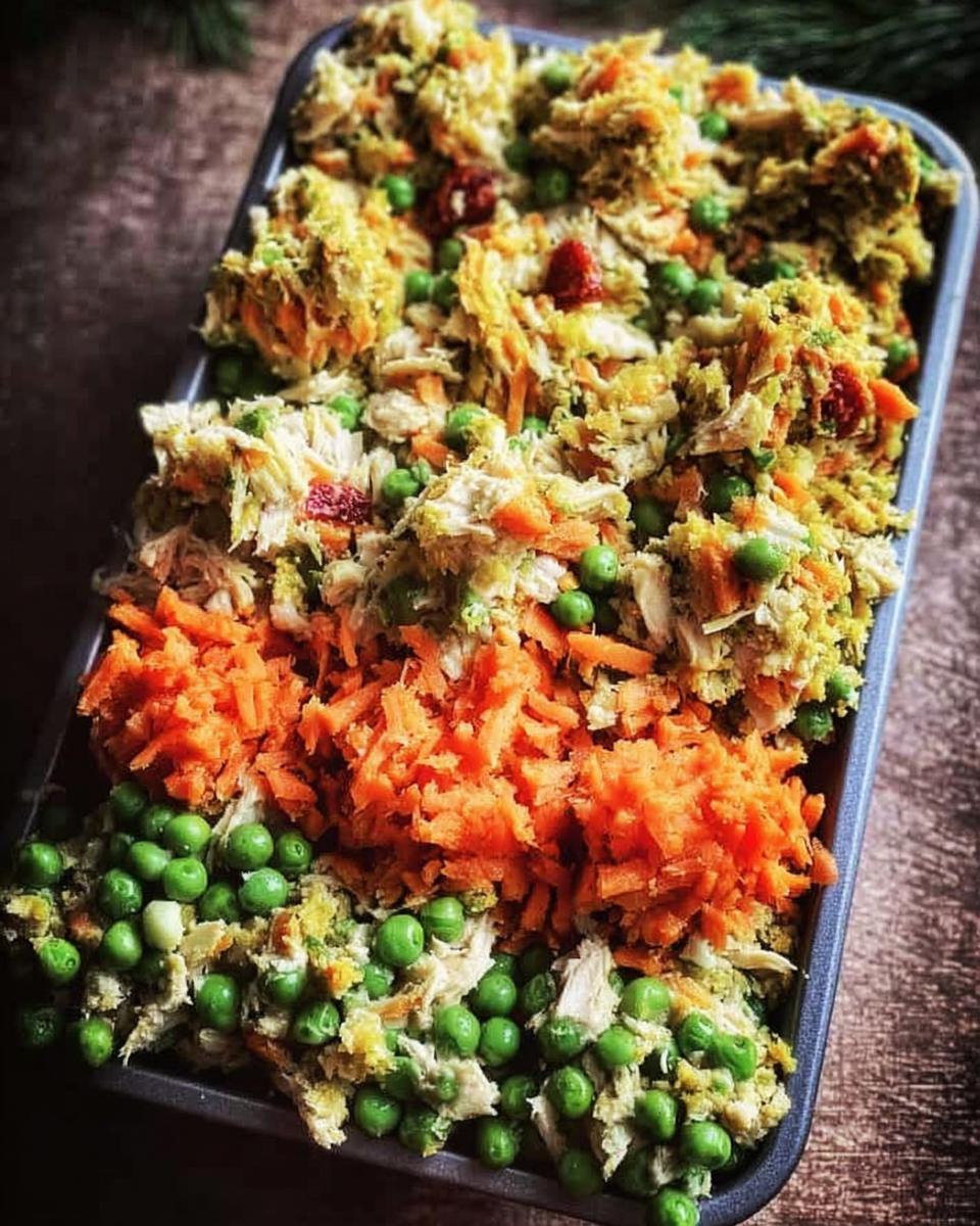 A metal tray filled with shredded chicken, bright green peas, and shredded carrots for Frozen Veggie Dog Meal Prep.