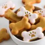 A close-up of bone-shaped Birthday Dog Cookies, some plain and some decorated with pink icing and gold paw prints.