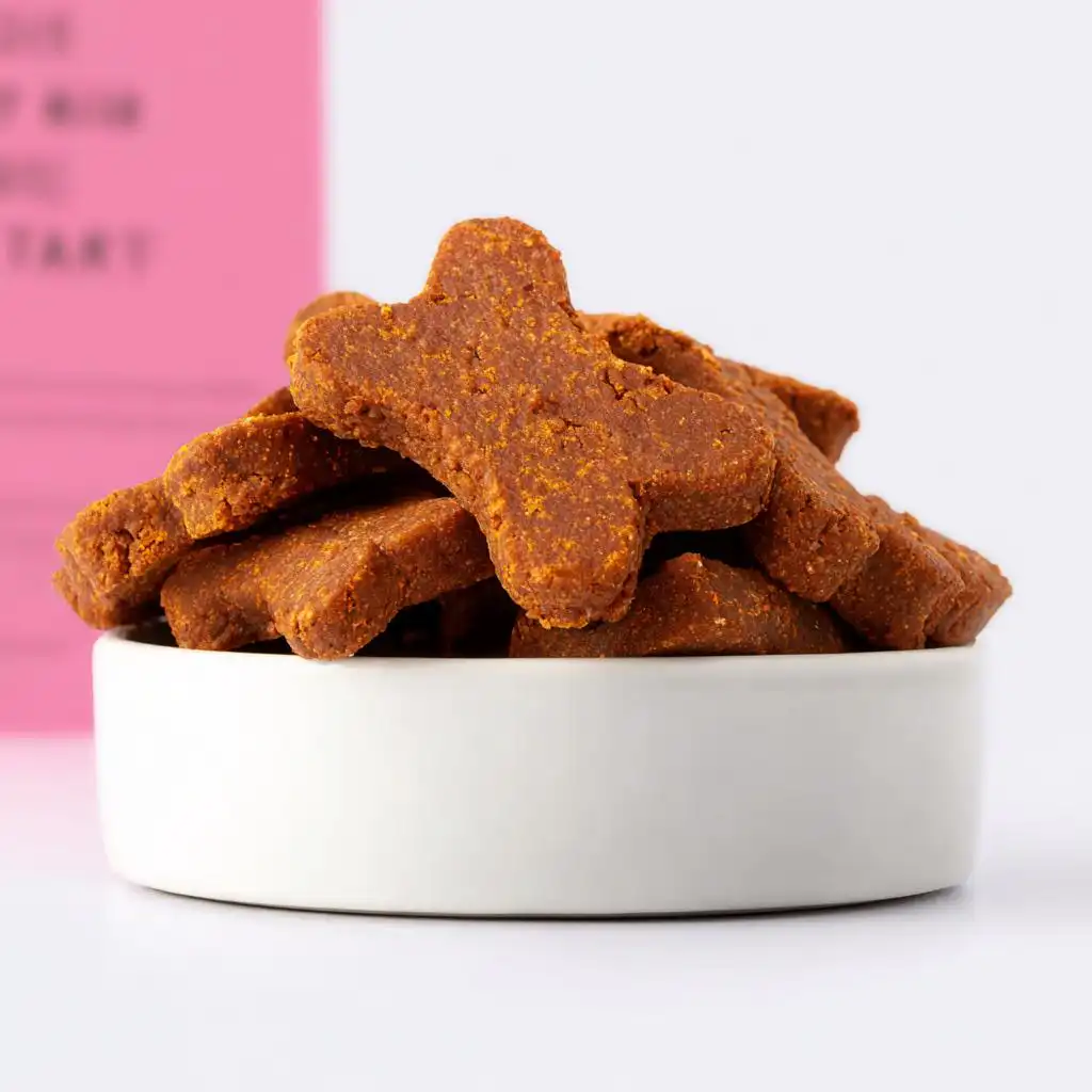A pile of homemade, bone-shaped Joint Support Dog Treats stacked in a small white ceramic bowl.