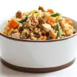 Close-up of a white and brown Homemade Dog Food Bowl filled with ground meat, rice, carrots, and green beans.
