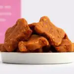 A close-up of bone-shaped Joint Support Dog Treats piled high in a small white bowl.